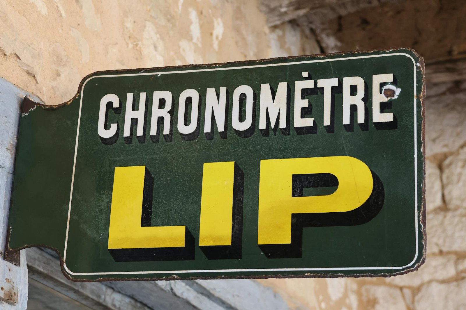Old French wall-mounted sign reading 'CHRONOMÈTRE LIP' in bold letters against a rustic background.