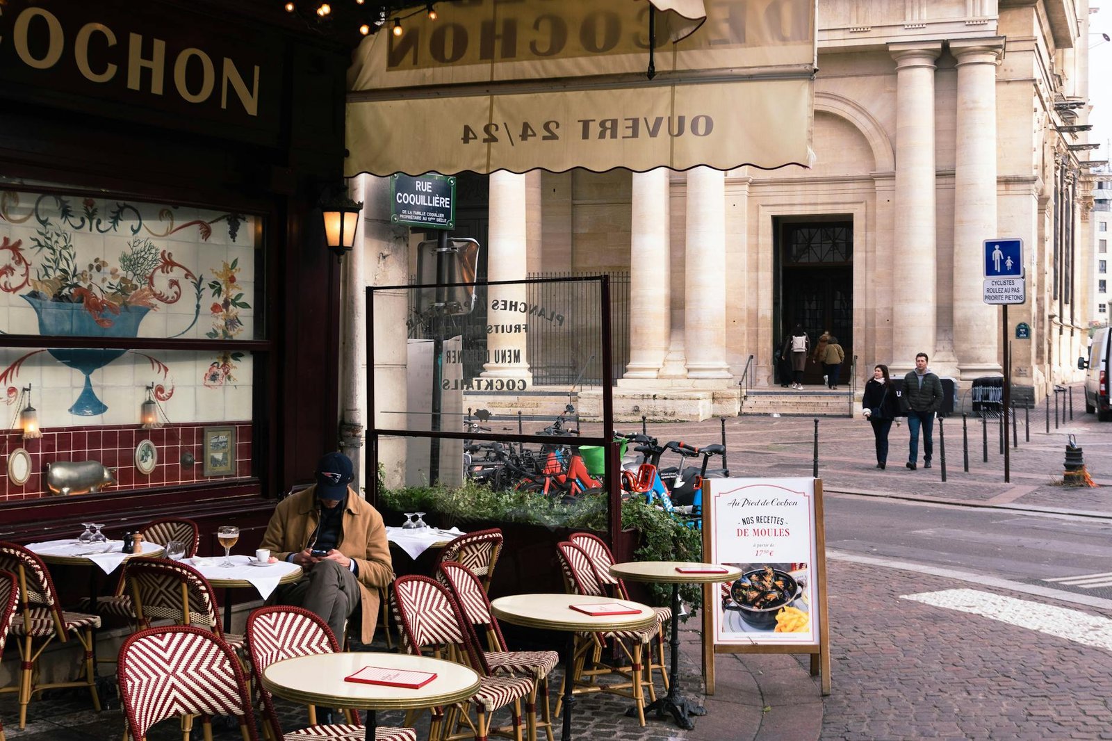 Outdoor café scene in Paris with patrons, street view, and historical architecture.