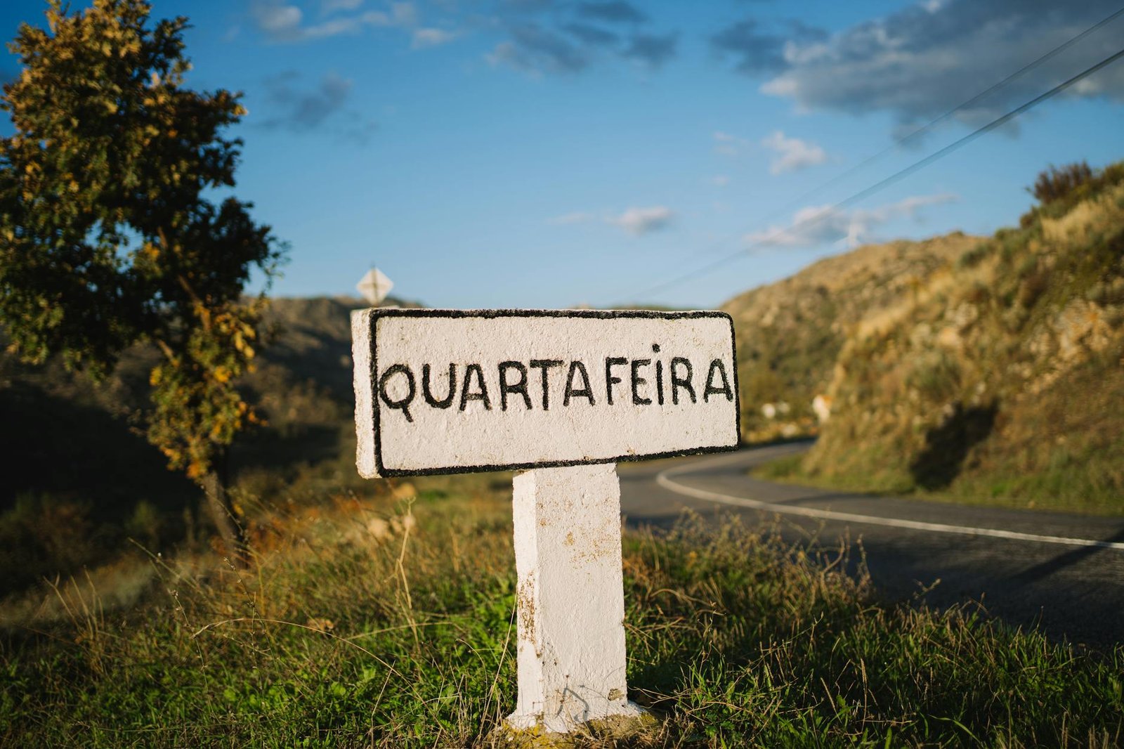 Rustic sign near winding road in Portuguese countryside at sunset.