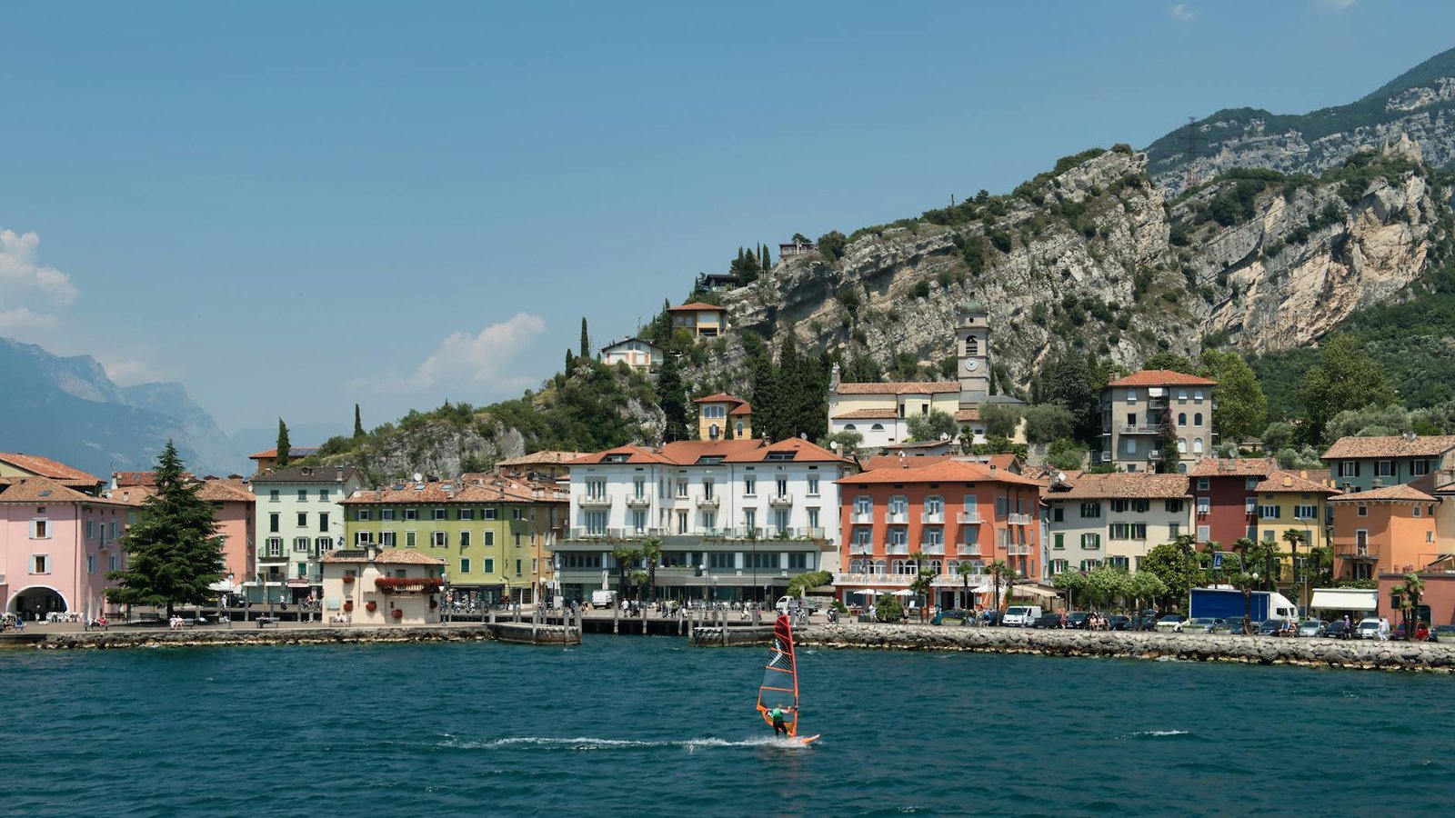 A beautiful view of Riva del Garda with colorful buildings and a windsurfing activity on Lake Garda, Italy.