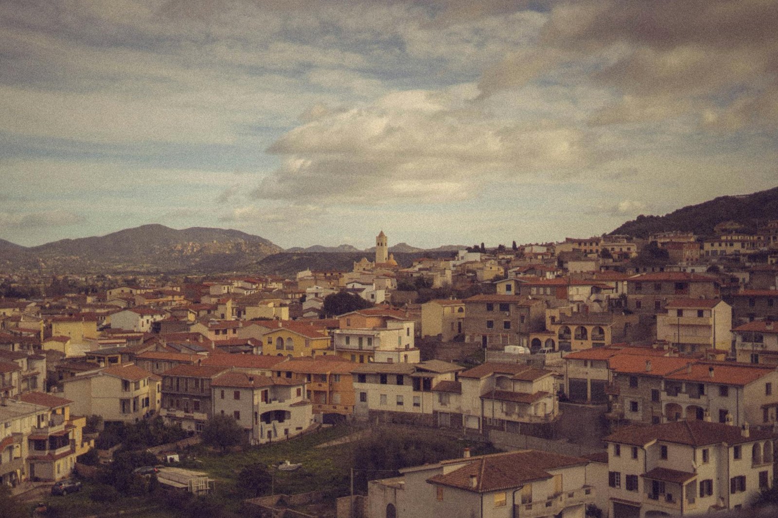 Aerial view of a charming Italian village with rustic houses and distant mountains under a cloudy sky.